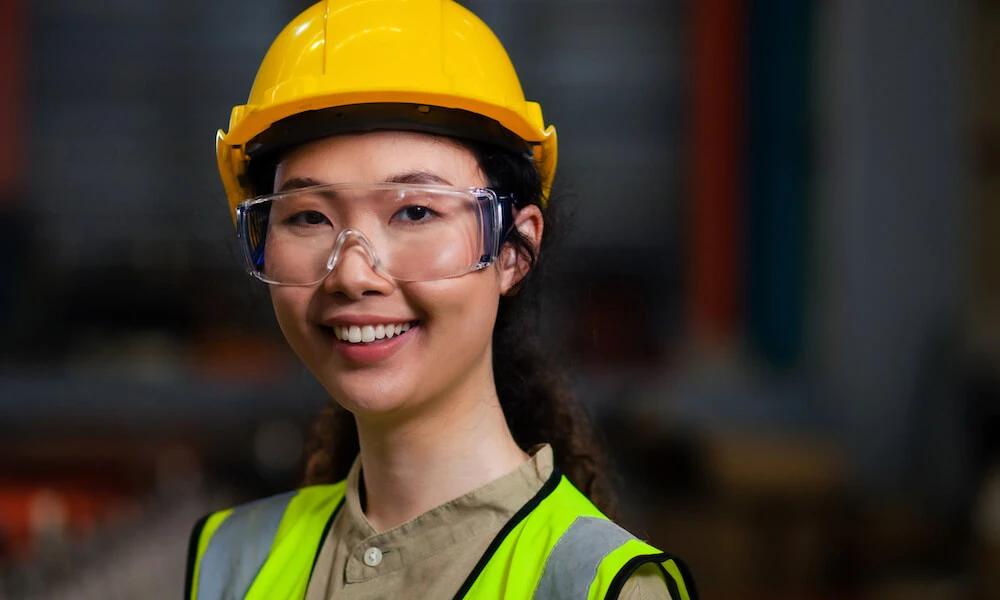 A young female asian construction worker wears her safety vest and hardhat and smiles